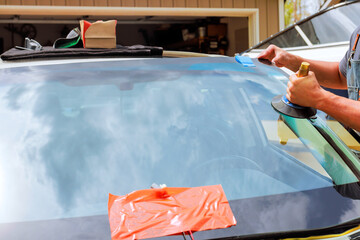 Windshield repair process underway in garage, applying adhesive tools during replace cracked...