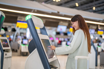 Confident woman traveler passenger with luggage using digital check in at airport kiosk, smart...