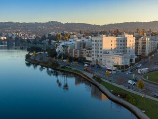 Fototapeta premium Lake Merritt in Oakland, California, USA, at sunrise. People walk along the path as cars and buses travel the road. Buildings line the street.