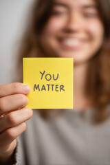 Smiling person holding a sunny yellow "You Matter" sticky note