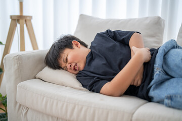 Portrait of sick unhappy little child asian boy touching belly stomach with suffering from stomach...