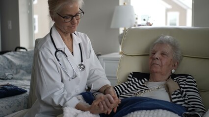 Obraz premium A mature woman relaxes in her chair, holding hands with a healthcare provider during a home visit. The atmosphere is calm and caring, fostering connection.