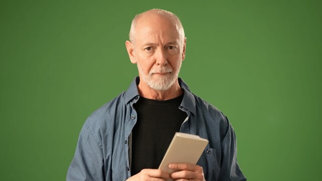 A mature man smiles gently while showing an okay hand gesture against a solid green background. He conveys a sense of warmth and positivity in this portrait.