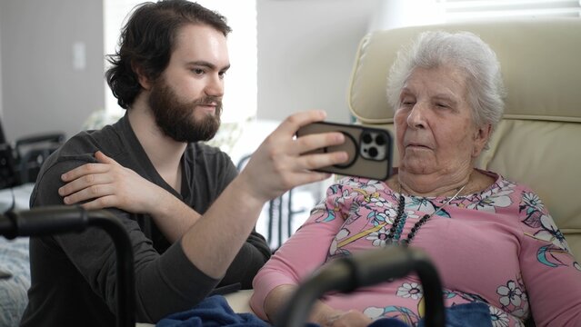 A grandson and grandmother enjoy a moment together, sharing memories on a smartphone, evoking happiness in their home filled with warmth and love.