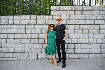 woman in green dress in hat and man in hat are near brick wall,