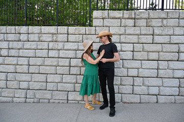 woman in green dress in hat and man in hat are near brick wall,
