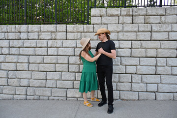 woman in green dress in hat and man in hat are near brick wall,