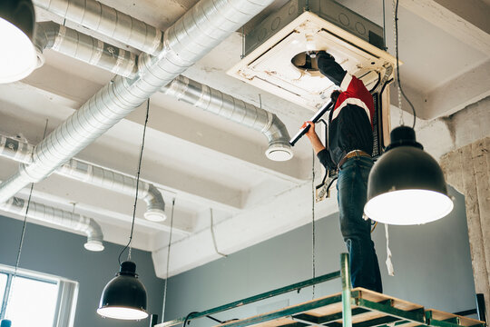 Technician performing maintenance on ceiling-mounted air conditioning unit in modern workspace