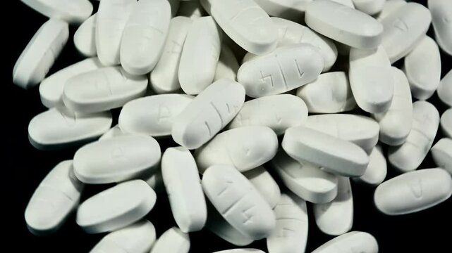 A pile of white pills in a pile rotating right to left. Close-up view on black background.