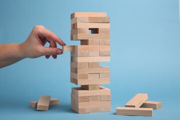 Lviv, Ukraine - December 04, 2023: Woman playing Jenga on light blue background, closeup