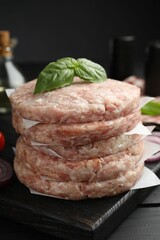 Fresh raw patties for burger and basil on black wooden table, closeup