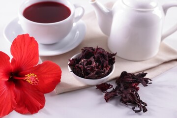 Tasty hibiscus tea, dry roselle sepals and beautiful flower on white table, closeup