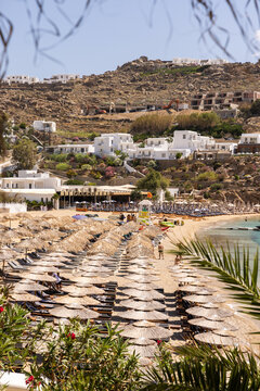 Wide angle view of beach club on Greek islands with lots of umbrellas and seating against a rocky landscape and blue sea.