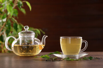 Cup of tasty green tea and teapot on wooden table