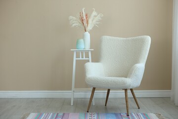 Comfortable armchair and table with vases near beige wall indoors, space for text