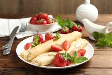 Tasty crepes with cream, strawberries and mint on wooden table, closeup