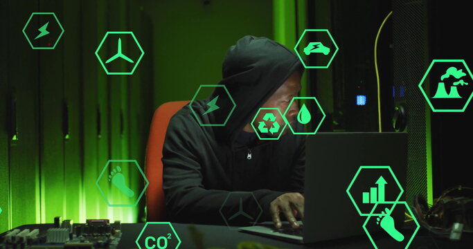 Typing IT pro in black hoodie managing servers in data center with laptop, circuitry, hexagon icons