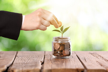 Investment for future profit. Woman putting coin into glass jar with seedling on wooden table...