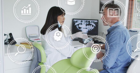 Dentist in lab coat and gloves consulting patient in clinic, with digital icons and X-ray monitor