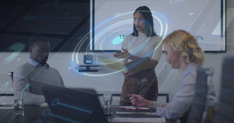 Pointing presenter in suit indicating charts on display in meeting room, with laptops