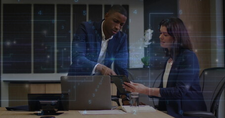 Leaning suited businessman pointing at tablet held by colleague in conference room, with laptop