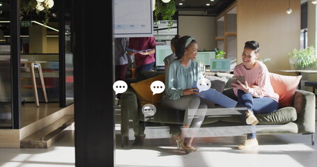 Discussing data two women wearing business attire reviewing tablet in office lounge, with reports