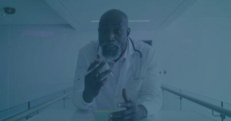 Leaning mature male doctor gesturing with pen and discussing folder in corridor, with stethoscope