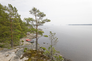 Inflatable boats rest on a rocky shore by a calm forest lake, surrounded by pine trees and distant...