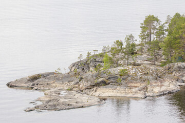 A quiet rocky island with sparse pine trees surrounded by calm lake waters, ideal for solitude,...