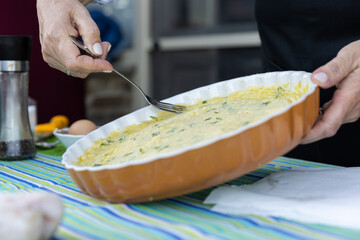 Woman smoothing a Greek potato pie in a ceramic dish with festive blue and green striped tablecloth.