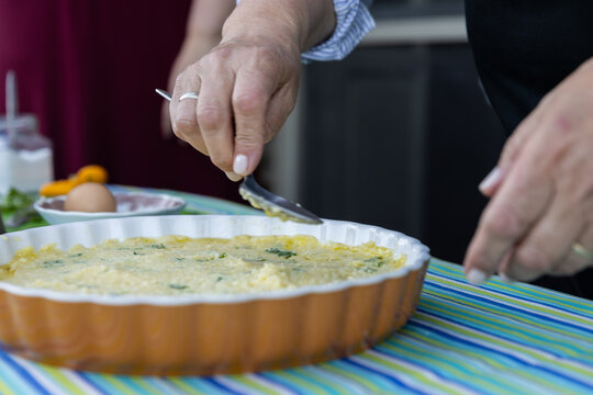 Woman smoothing a Greek potato pie in a ceramic dish with festive blue and green striped tablecloth.