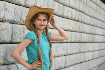 beautiful blonde girl in a hat is near a brick wall,