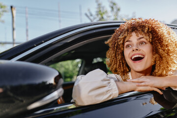 curly woman looking excitedly out of car window, sunny day, casual beige blouse, outdoor, joyful...