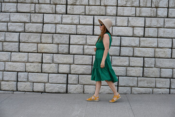 woman in green dress in hat is near brick wall,