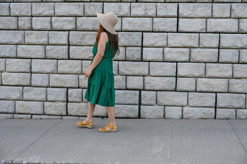 woman in green dress in hat is near brick wall,