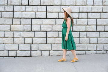 woman in green dress in hat is near brick wall,