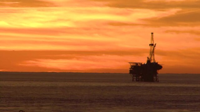 An offshore oil rig is sihouetted against an orange sunset near the UCSB campus near Santa Barbara, California.