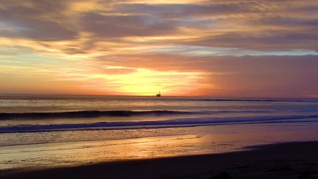 Purple and orange predominate in this sunset on the beach and an offshore oil drilling rig is silhouetted on the horizon in this scene by the UCSB campus near Santa Barbara, California. 