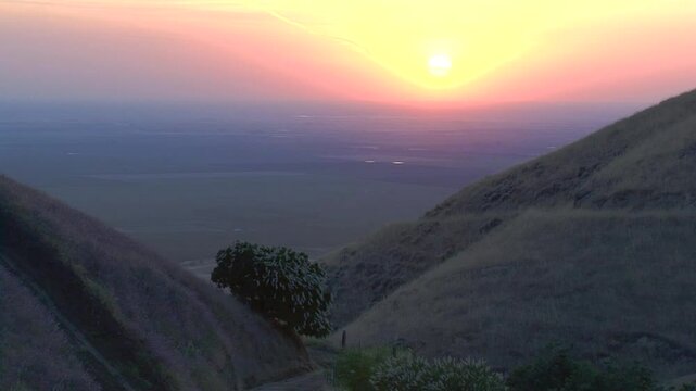 The sun sets over California's Great Central Valley as seen from the foothills of the Tehachapi Mountains outside of Bakersfield, where California Buckeye trees bloom.