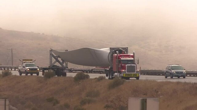 A diesel truck tows an oversized trailer bearing a single, incredibly large electrical windmill blade down Interstate Highway 5 near Frazier Park, California.