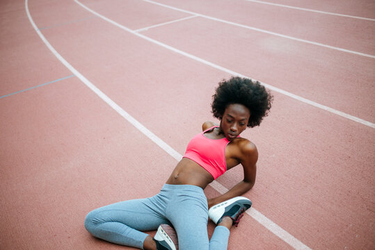 Young female athlete stretching legs on running track