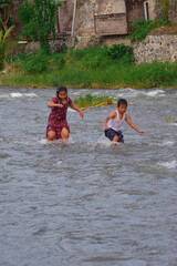 A boy and girl confidently step through the flowing water, moving against the current while...