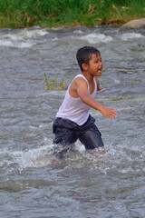 A boy walks steadily through the rushing river water, showing confidence and joy, surrounded by rippling currents and lush greenery.