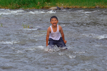 A young boy stands proudly with a confident expression, resisting the strong current of the river,...