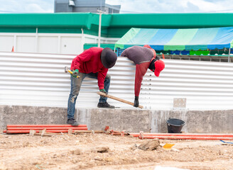Two workers are working together to adjust the plate by tapping it with a wooden block.