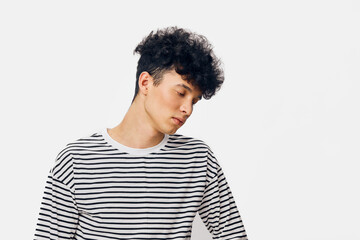 young man in striped shirt looking down pensively with curly hair on white background, casual pose...