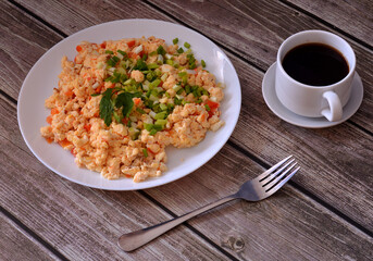 Freshly cooked egg omelette with tomatoes, green onions and parsley, cup of black coffee and fork on wooden table.