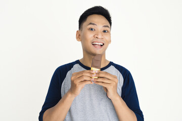 A cheerful person holding and enjoying a chocolate bar, wearing casual clothing, showing happiness and delight on a plain white background.
