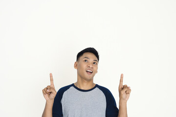 Cheerful young man gesturing upward with enthusiasm, wearing casual clothing and standing against a plain background, perfect for concepts of ideas, creativity, or inspiration.