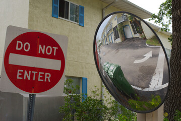 Do Not Enter Sign with Nearby Surveillance Mirror Reflecting Building.Urban setup featuring a...